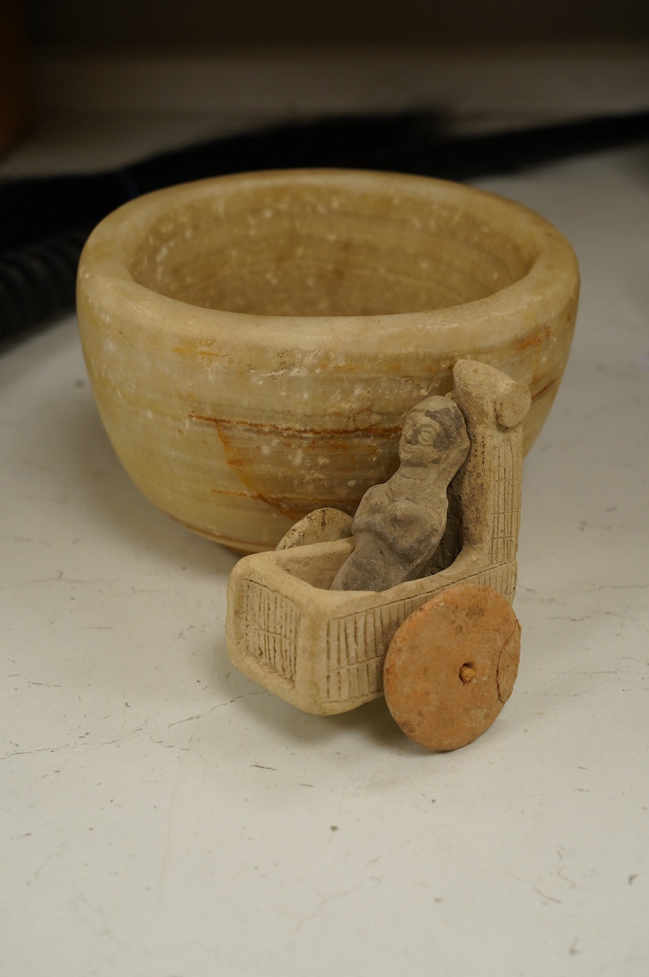 An alabaster mortar, possibly Ancient Egyptian, 17cm diameter, the handles ground off and a terracotta figure with chariot, possibly Mesopotamian. Condition - fair, restoration to chariot